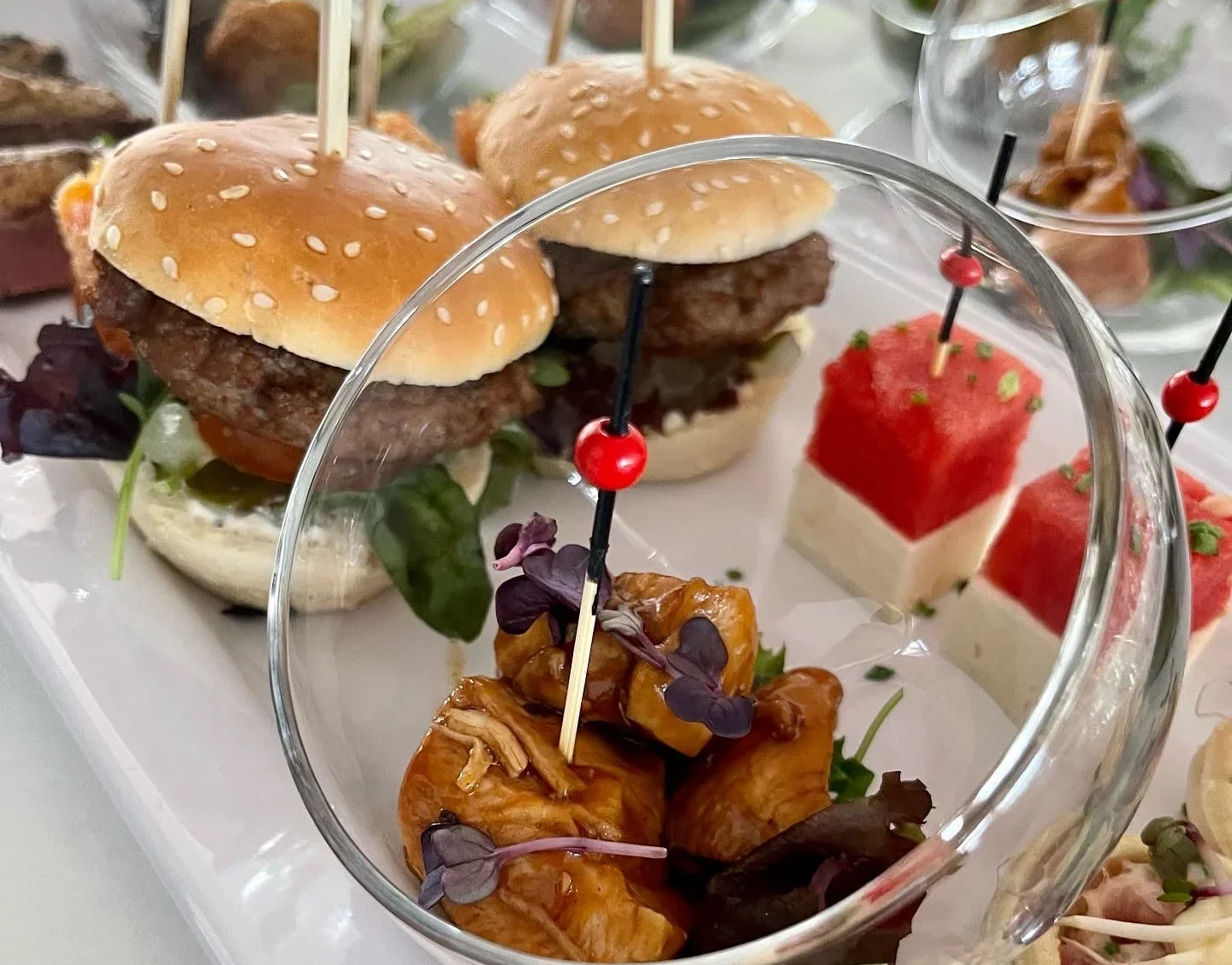 Glasschale mit Fingerfood neben Mini-Burgern und Tartelettes auf einer Catering-Platte