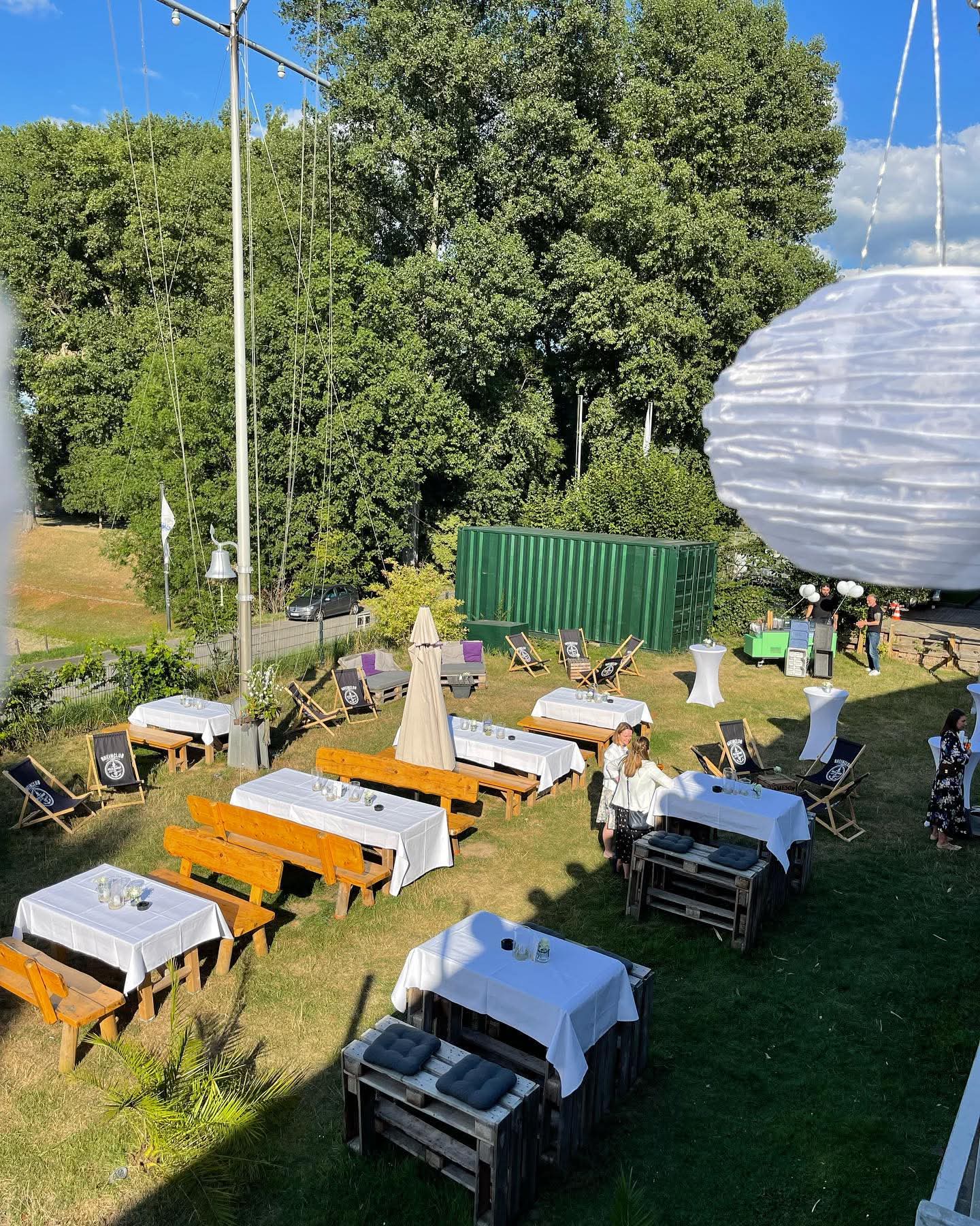Gedeckte Tische, Holzbänke und Liegestühle im Garten des Rheinclub 297 bei Sonnenschein