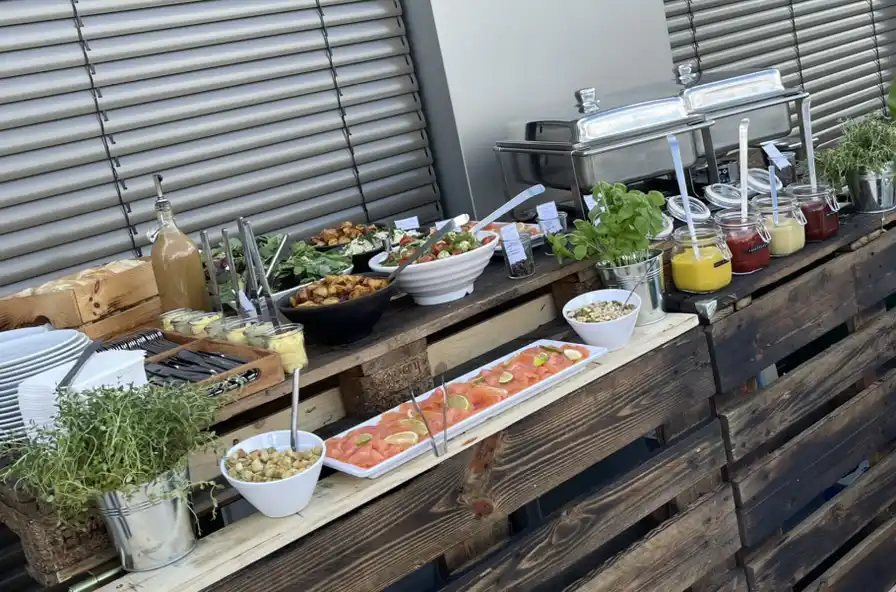 Buffet auf Holzpaletten im Freien mit Salaten, Lachs, Dips und Warmhaltebehältern