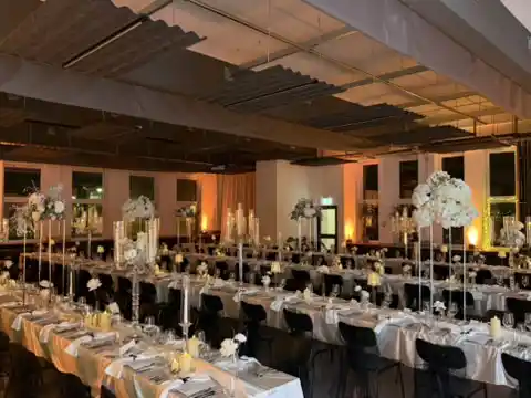 Festlicher Saal mit langen, weiß eingedeckten Tafeln, hohen Blumengestecken und Kerzenleuchtern