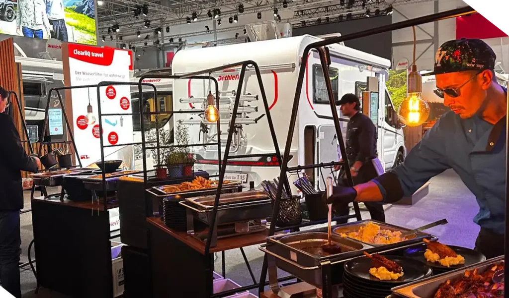 Koch richtet an einer Catering-Station auf einem Messestand warme Speisen auf Tellern an